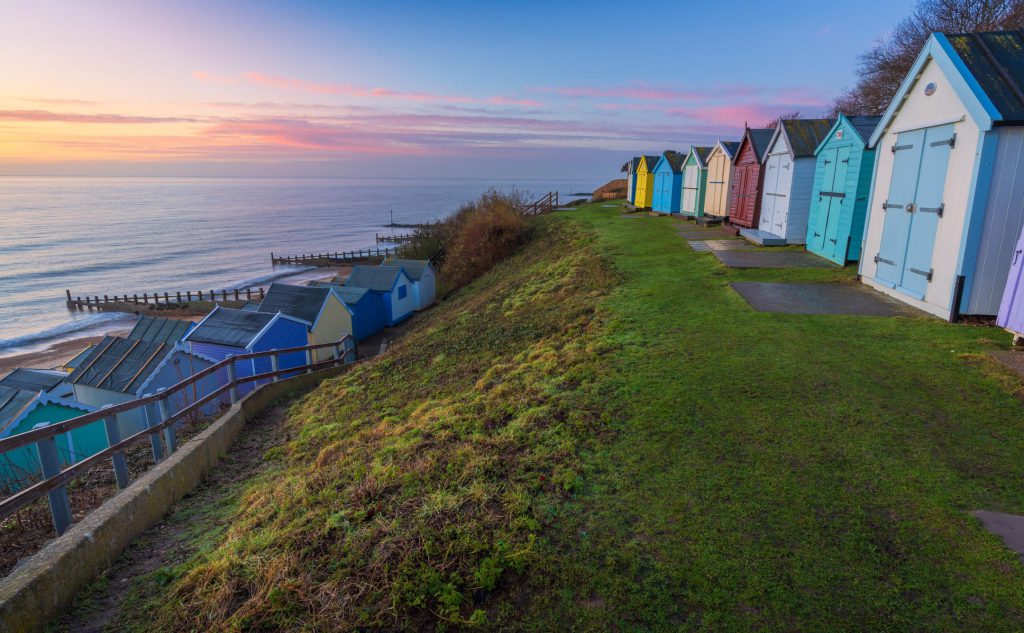 Colourful beach huts along a grassy cliff at sunrise, UK