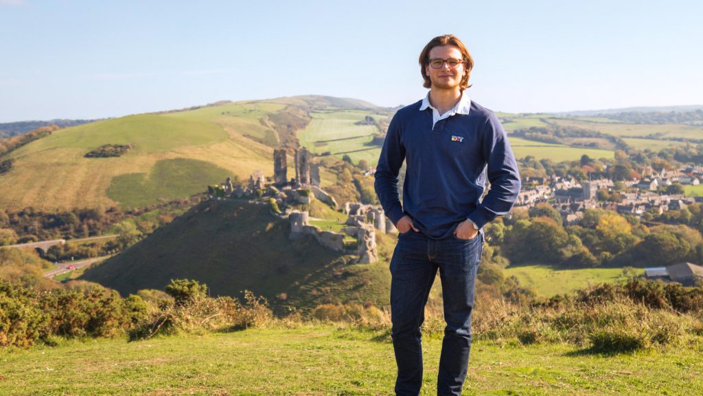 Young man standing on a hill overlooking Corfe Castle, Dorset, England