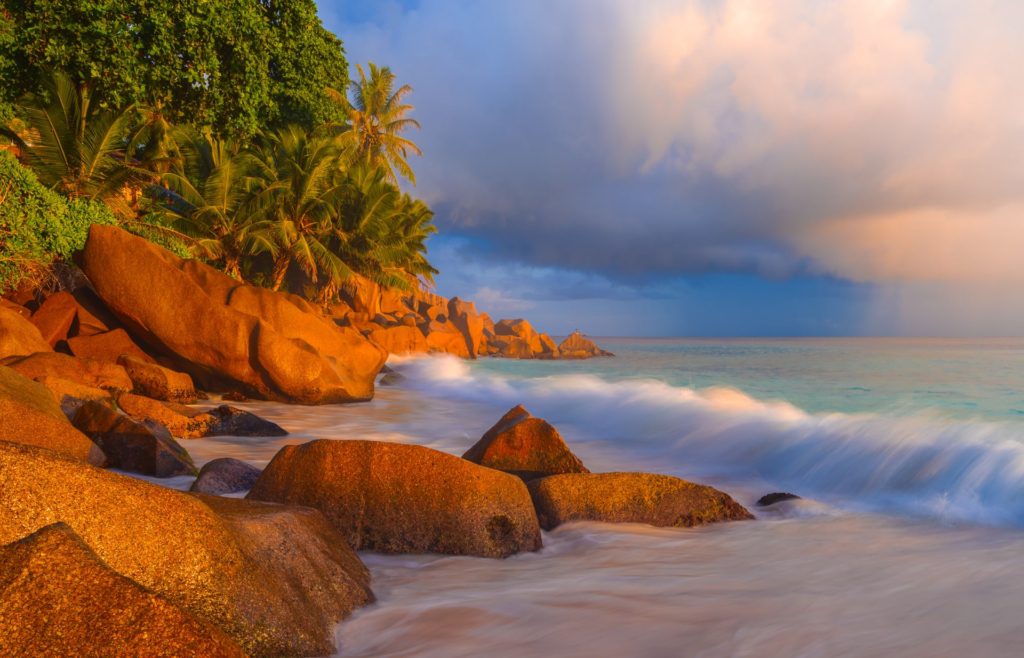 Stormy sunrise illuminating rocks and palm trees at Anse Patates, La Digue, Seychelles