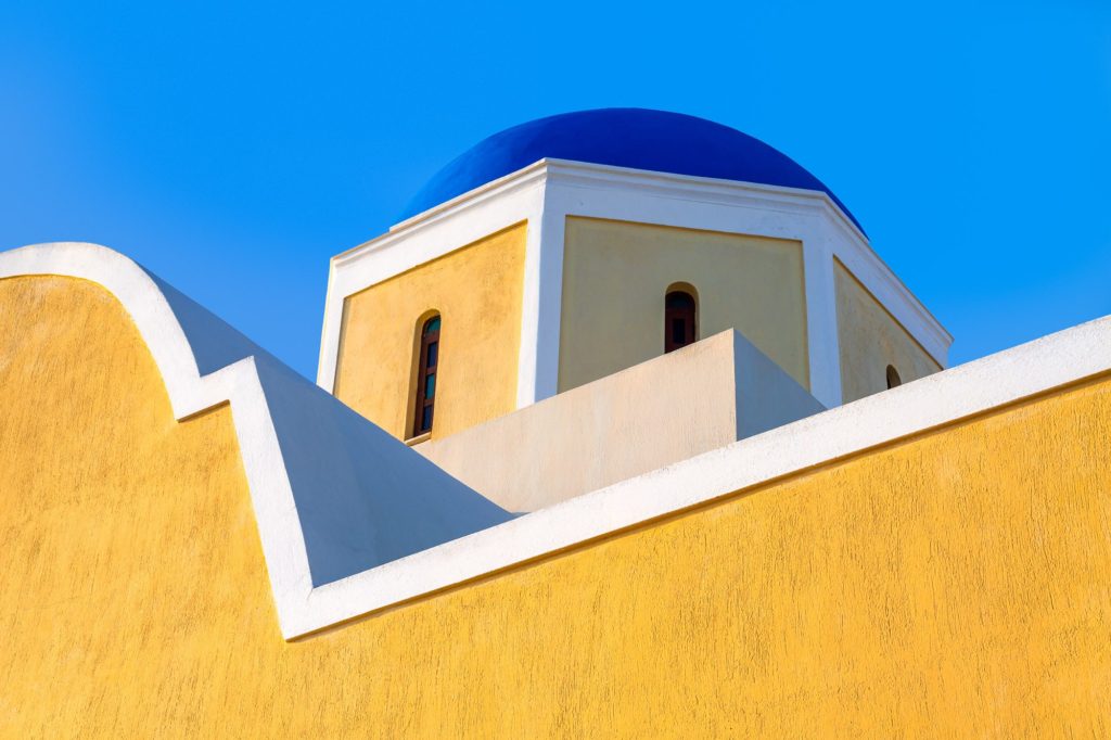Bright yellow building with blue dome in Oia, Santorini, Greece