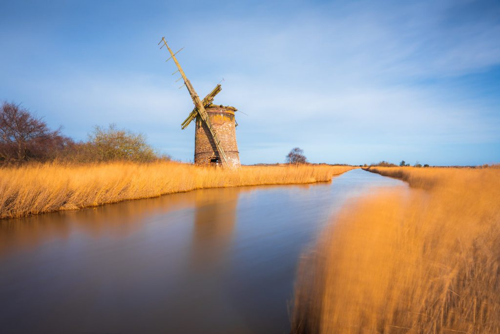 Brograve Mill surrounded by tall grasses and a winding waterway, Norfolk, England