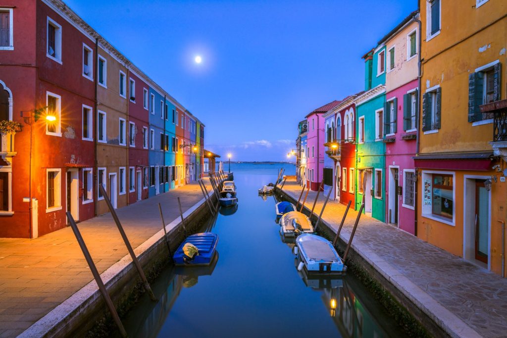 Colourful buildings lining a canal at blue hour in Burano, Italy