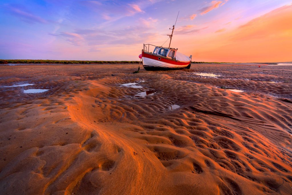 Boat stranded on sandy shore at low tide, Burnham Overy Staithe, Norfolk, England
