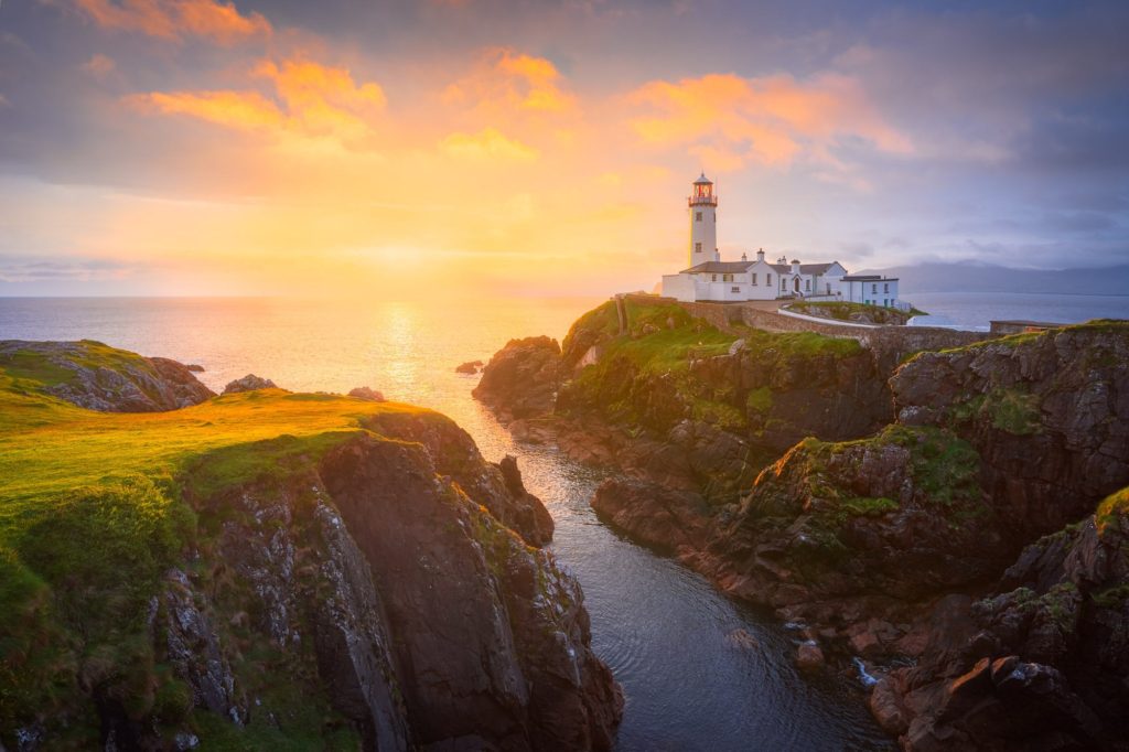 Lighthouse perched on rocky cliffs at sunrise, Ireland