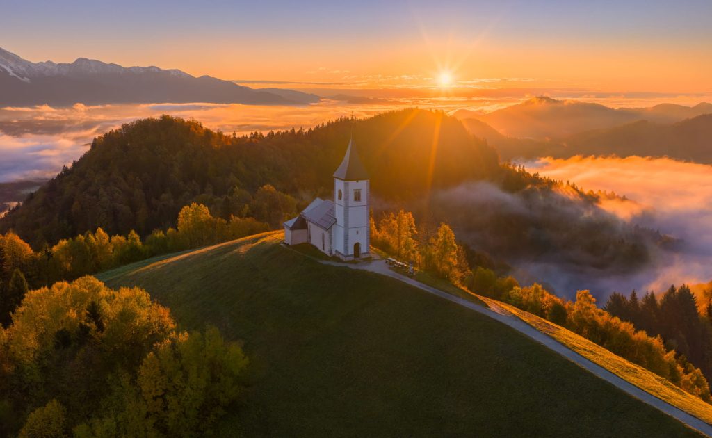 Jamnik church illuminated by sunrise, Slovenia's mountainous landscape