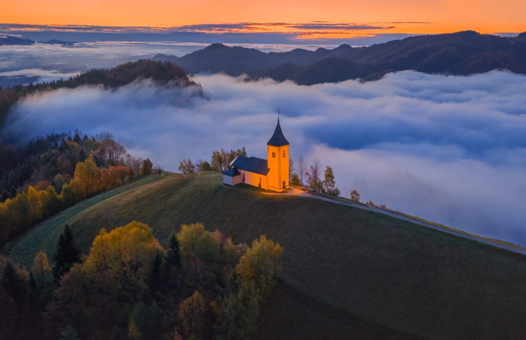 Jamnik church illuminated at sunrise above misty hills, Slovenia