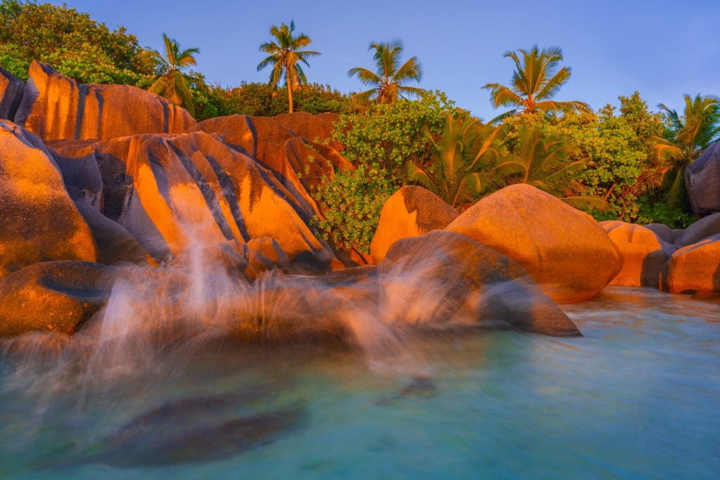 Sunset illuminating crashing waves on rocky shore, La Digue, Seychelles