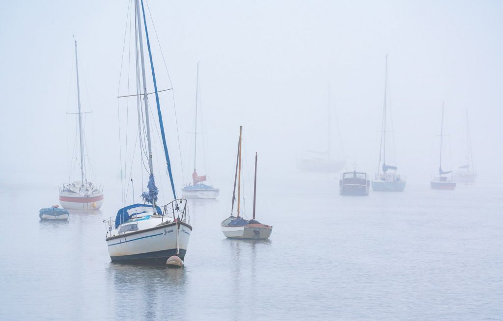 Manningtree boats anchored in foggy morning waters, Essex, England