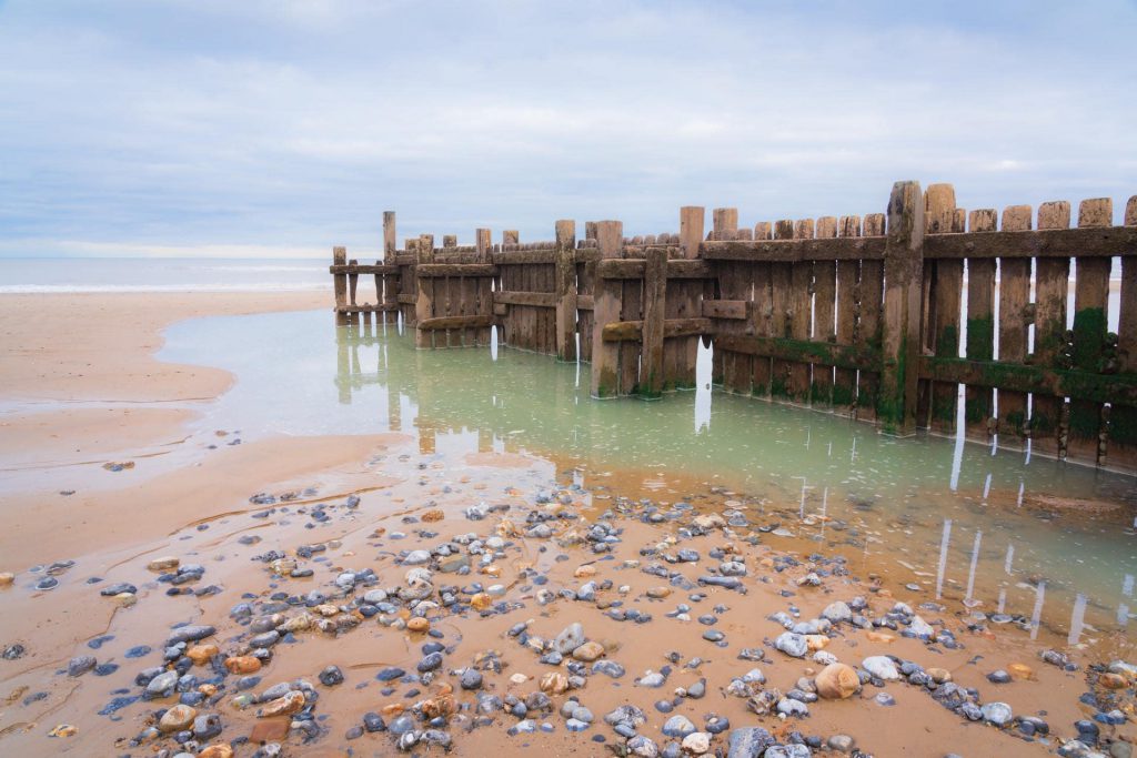 Overstrand beach landscape with wooden groynes and pebbled shore, Norfolk, England