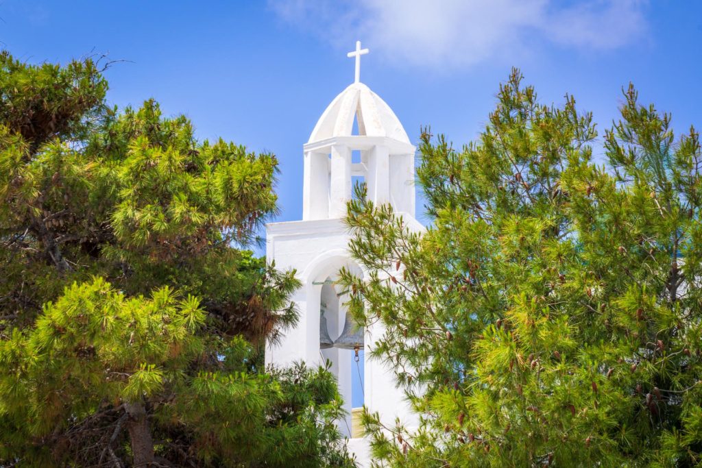 White church tower peeking through green trees in Santorini, Greece