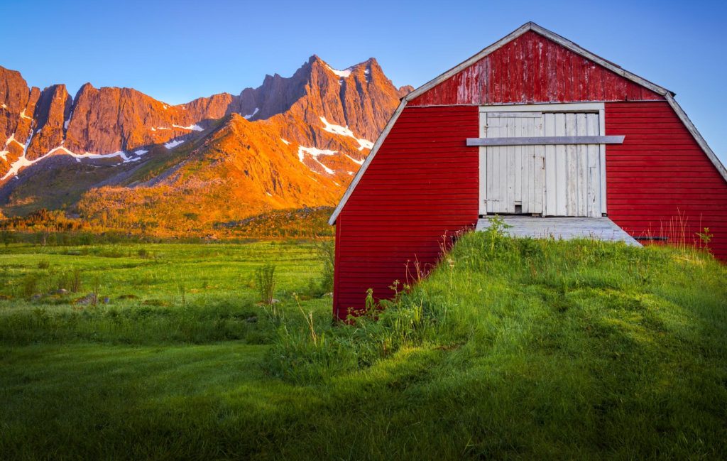 Red barn against mountainous landscape in Senja, Norway at midnight sun