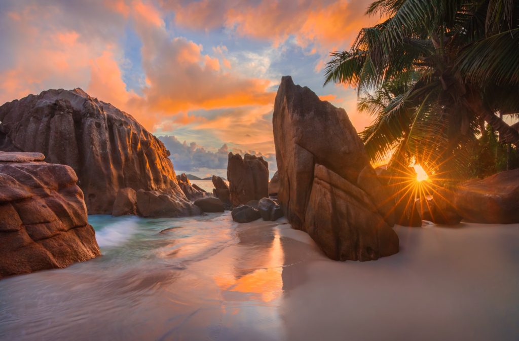 Sunrise over Anse Patates beach with rocks and palm trees, La Digue, Seychelles