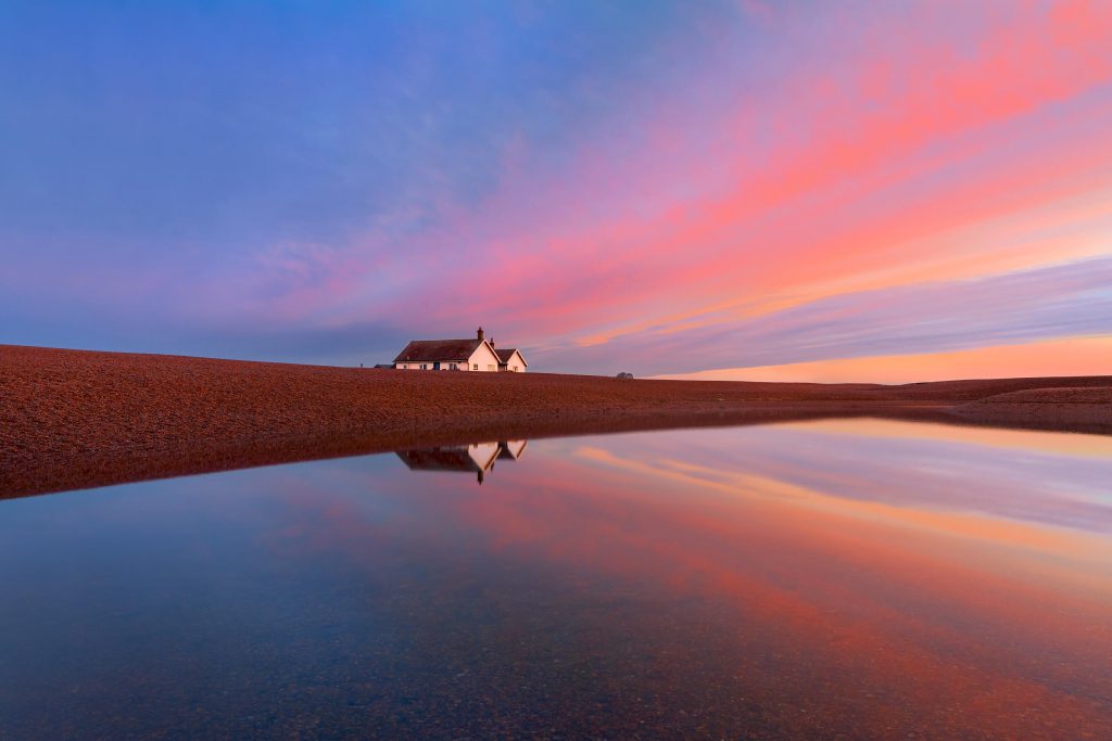 Cottages at sunrise reflecting in water, Shingle Street, Suffolk, England