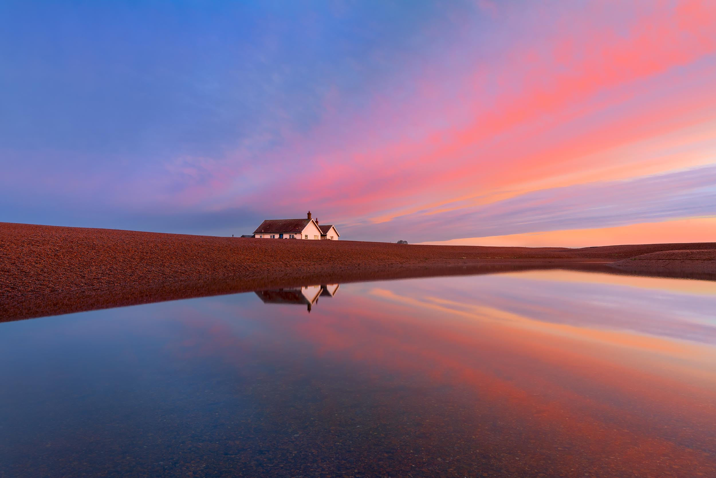 Cottages at sunrise reflecting in water, Shingle Street, Suffolk, England