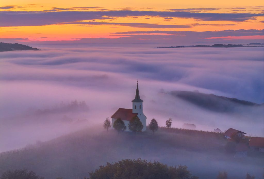 Church surrounded by misty clouds at sunset, Slovenia
