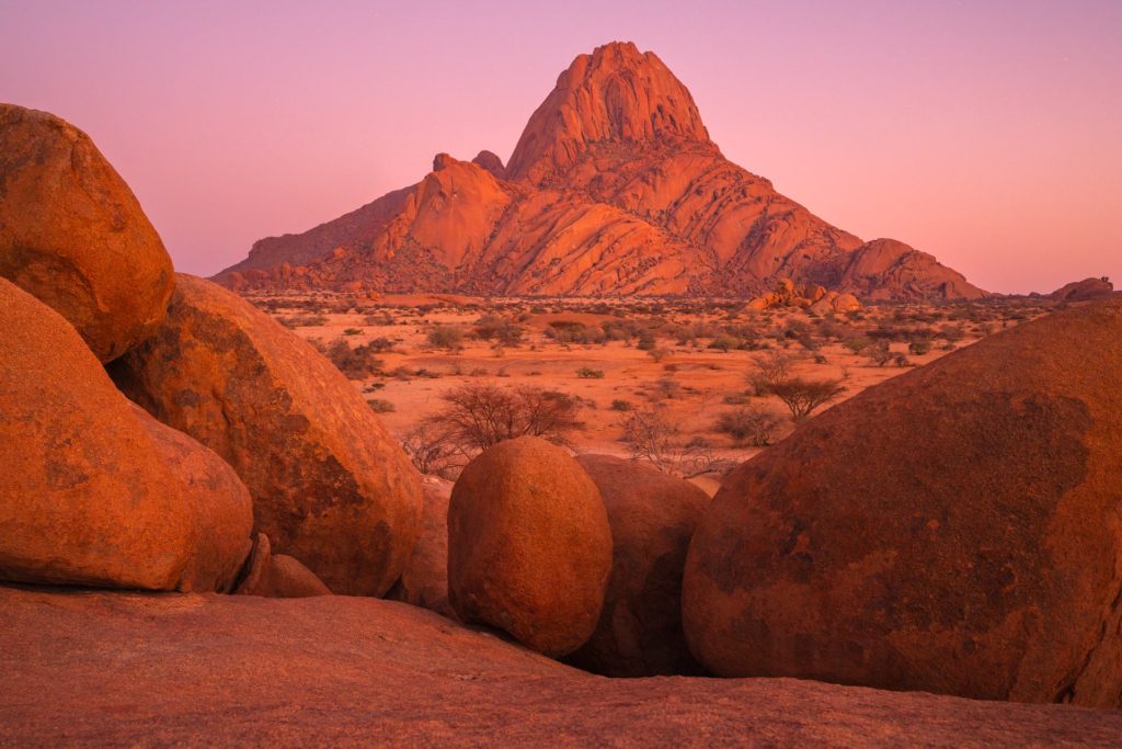 Sunrise glow over Spitzkoppe mountain, Namibia with foreground boulders