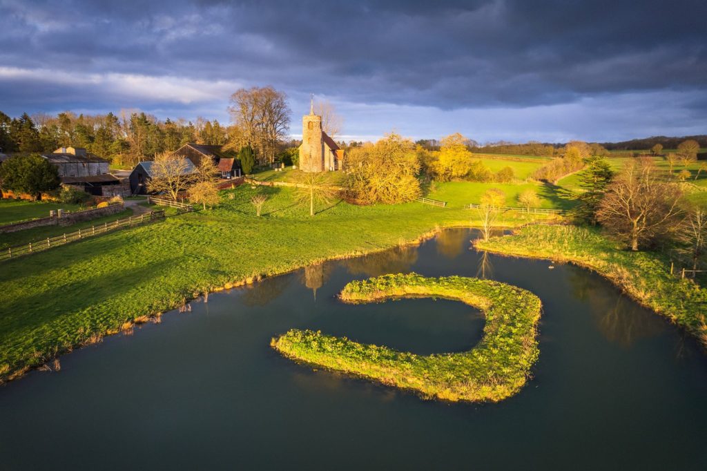 Stormy sunset over a Suffolk landscape with a church and pond