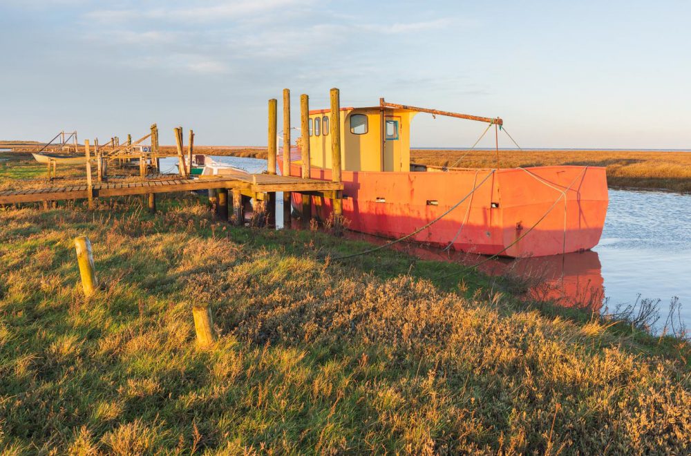 Old boat moored at Old Thornham Harbour with golden sunlight