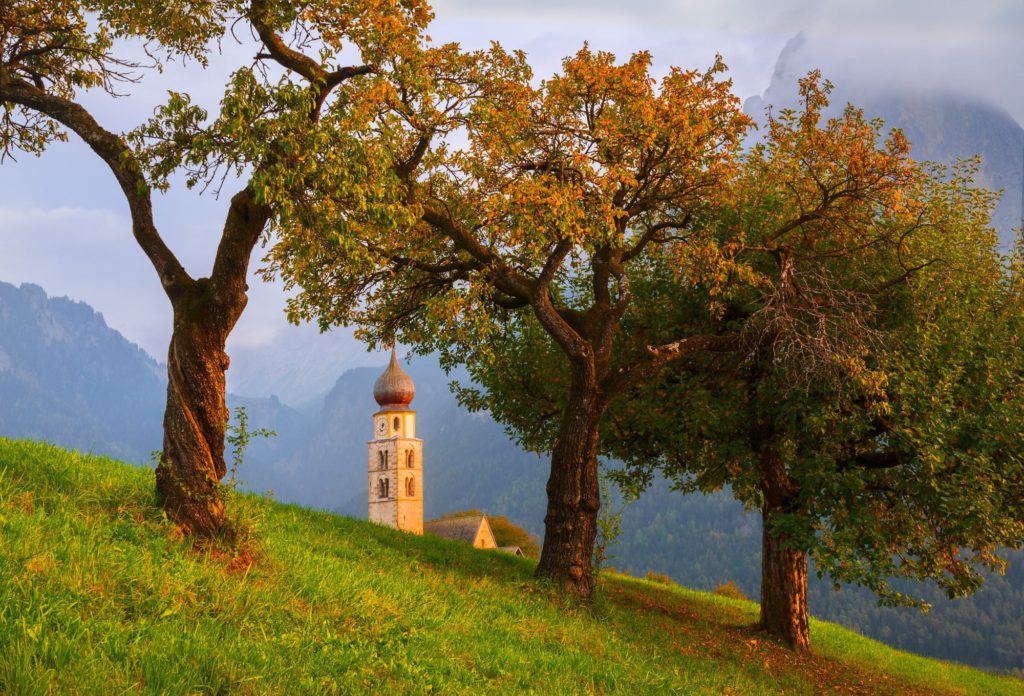 Valentin Church surrounded by autumn trees at sunset, Dolomites, Italy