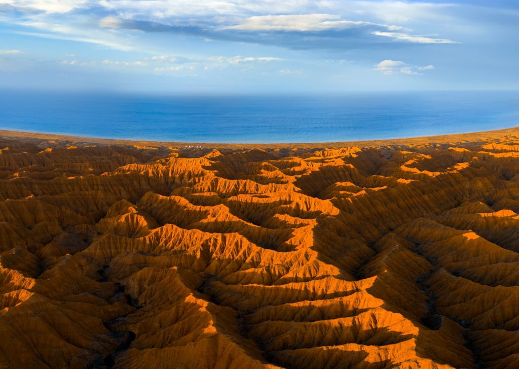 Stunning view of orange-hued valleys meeting the blue lake and sky